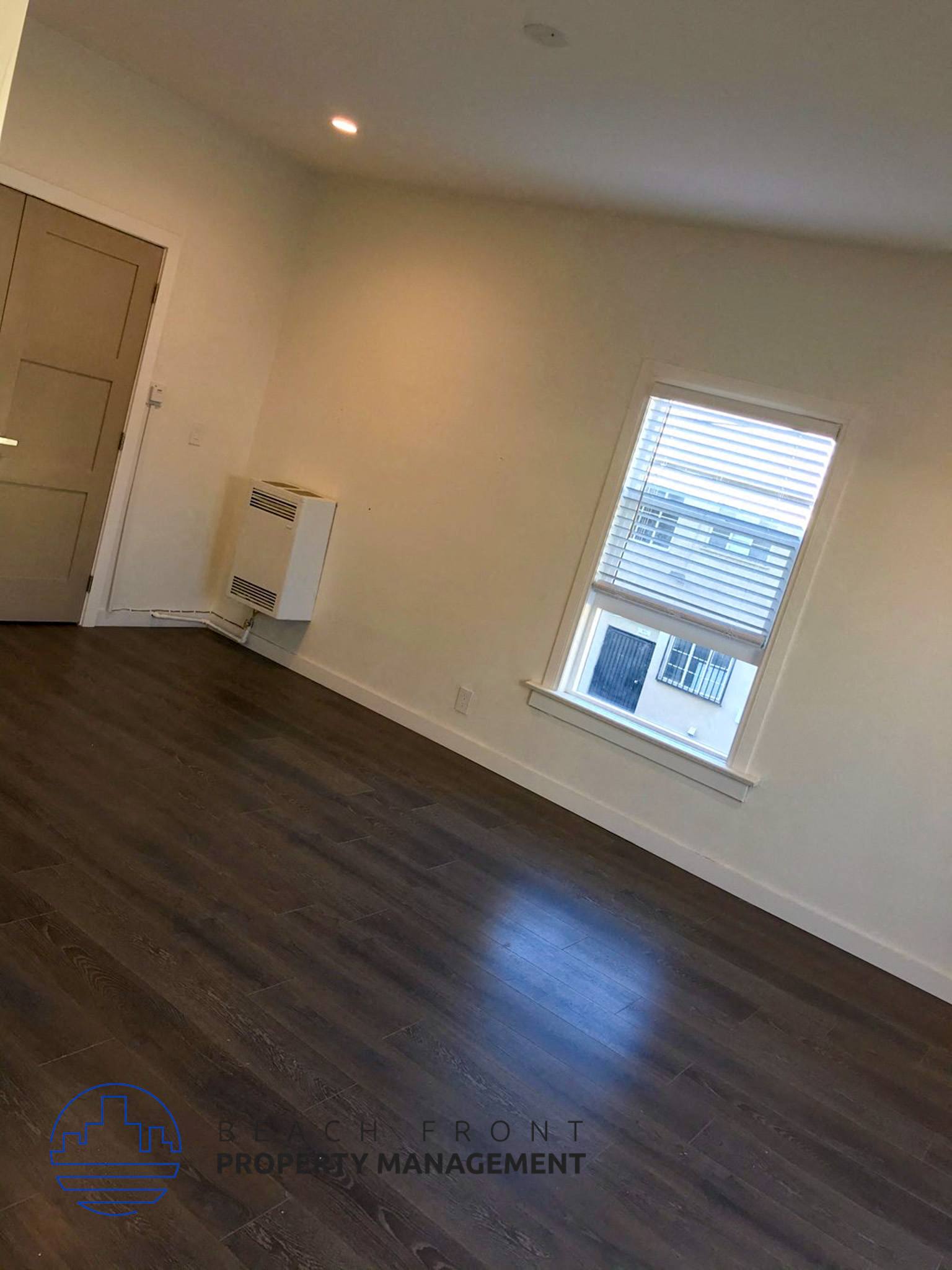 the living room of a home with a window and wooden floors